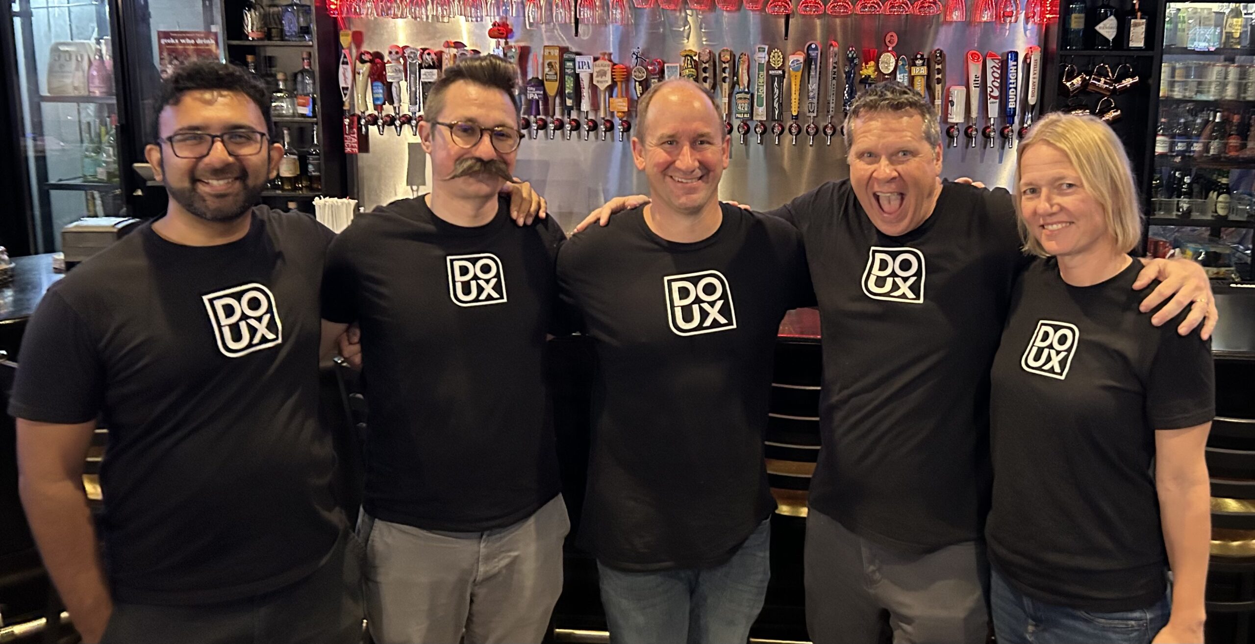 The 5 co-organizers of the meetup pose for a photo wearing black DOUX shirts.